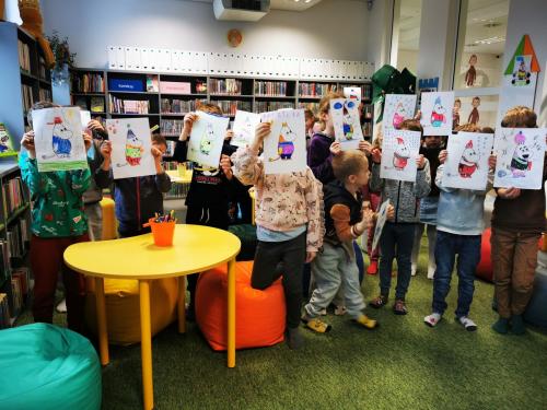 14 dzieci prezentują wykonane podczas lekcji bibliotecznej rysunki