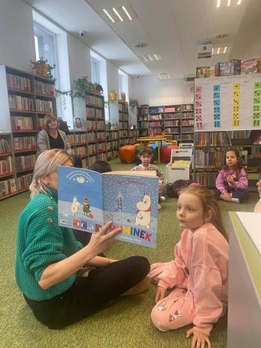 6 dzieci słuchają a bibliotekarka Asia czyta Muminki podczas lekcji bibliotecznej
